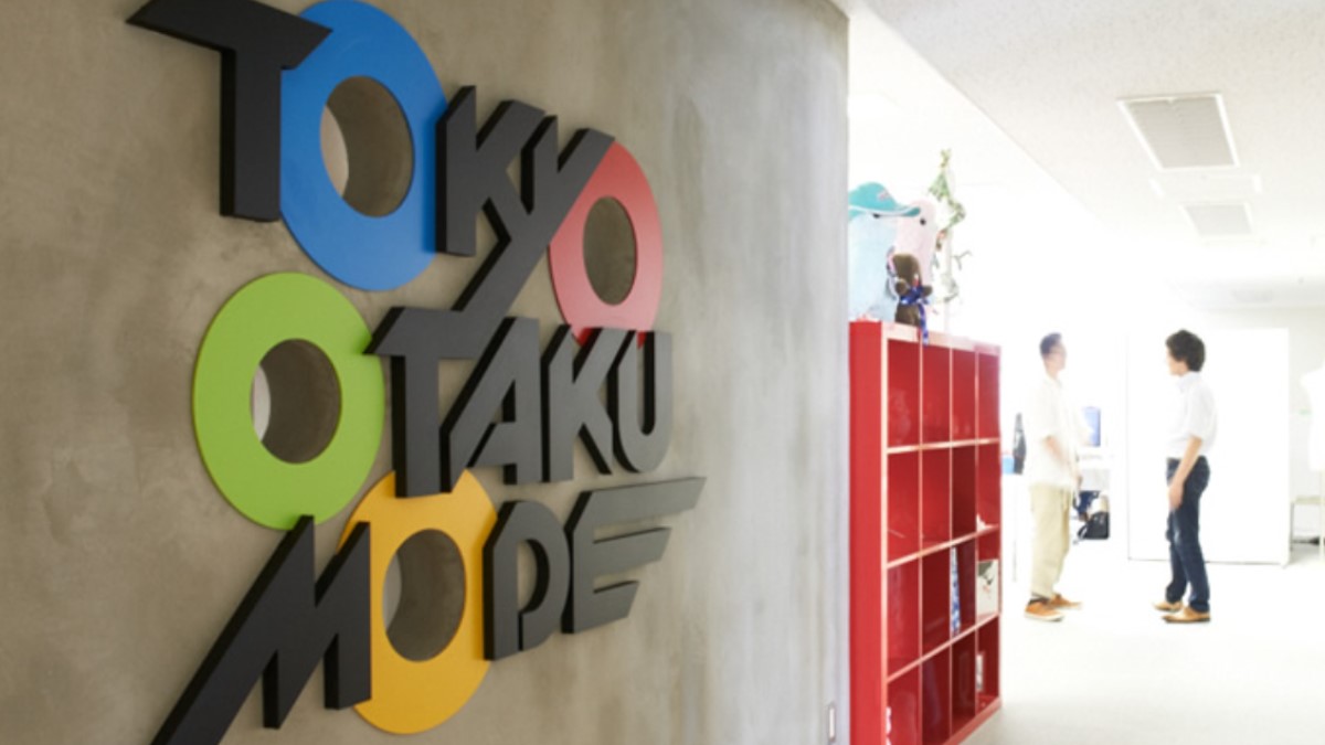 The Tokyo Otaku Mode logo on a wall. Two employees stand nearby.